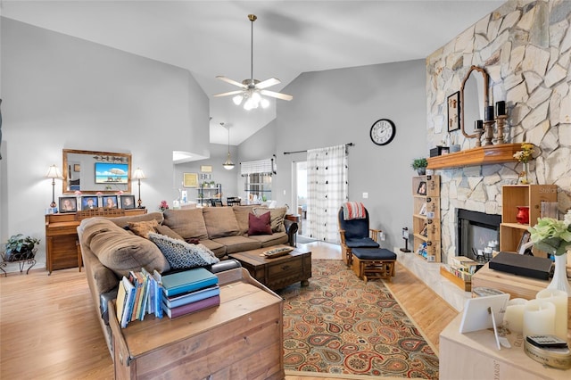 living room with ceiling fan, a stone fireplace, high vaulted ceiling, and light wood-type flooring