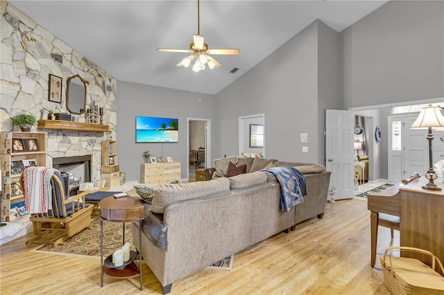 living room with a stone fireplace, high vaulted ceiling, ceiling fan, and light wood-type flooring