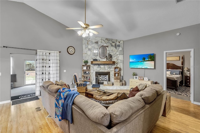 living room featuring ceiling fan, a stone fireplace, vaulted ceiling, and wood-type flooring