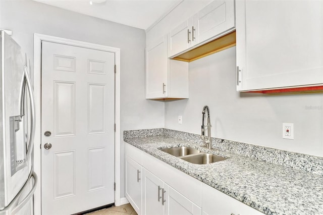 kitchen with light stone countertops, white cabinets, sink, and stainless steel refrigerator