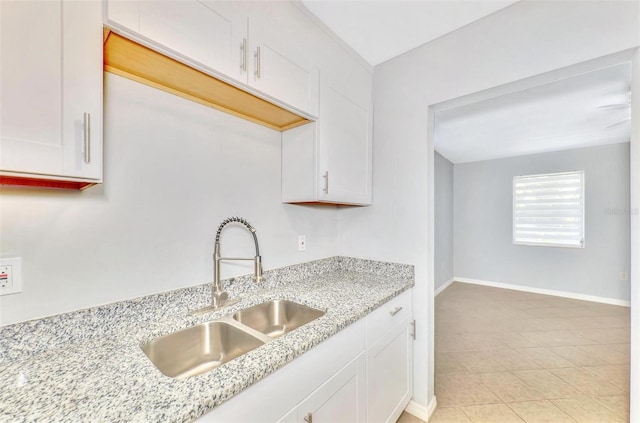 kitchen featuring white cabinetry, light stone counters, light tile patterned floors, and sink