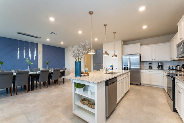 kitchen featuring white cabinets, pendant lighting, stainless steel appliances, and a center island with sink