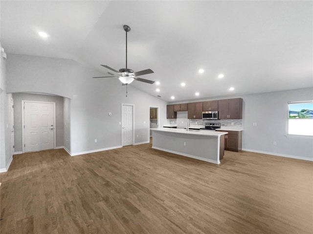 kitchen featuring ceiling fan, lofted ceiling, a kitchen island with sink, appliances with stainless steel finishes, and hardwood / wood-style floors