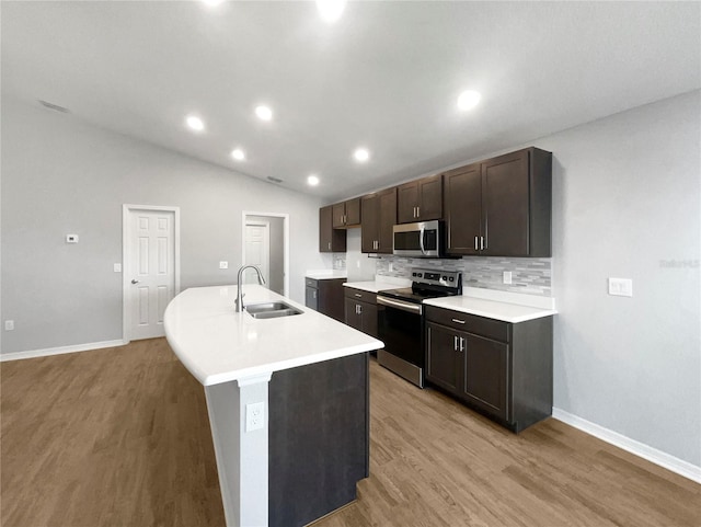 kitchen with appliances with stainless steel finishes, an island with sink, lofted ceiling, light hardwood / wood-style flooring, and sink