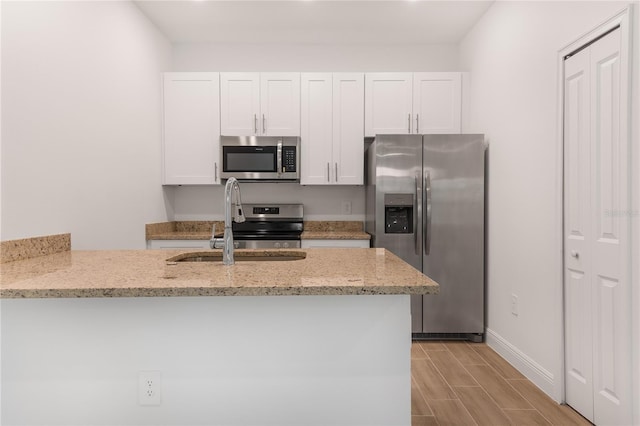 kitchen with white cabinets, kitchen peninsula, appliances with stainless steel finishes, light stone countertops, and light hardwood / wood-style floors