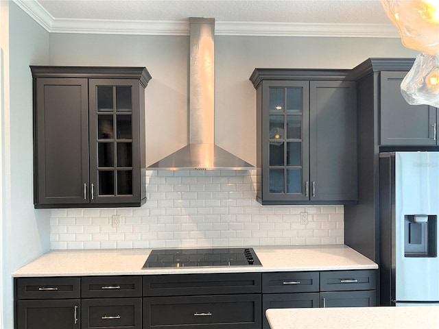 kitchen with wall chimney exhaust hood, backsplash, ornamental molding, black stovetop, and stainless steel fridge