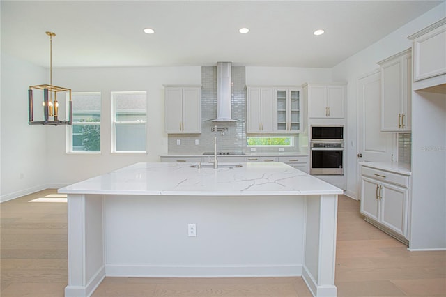 kitchen featuring an island with sink, light stone counters, and wall chimney range hood