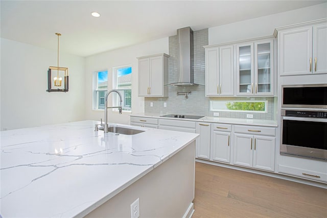 kitchen featuring sink, light hardwood / wood-style flooring, wall chimney range hood, white cabinetry, and appliances with stainless steel finishes