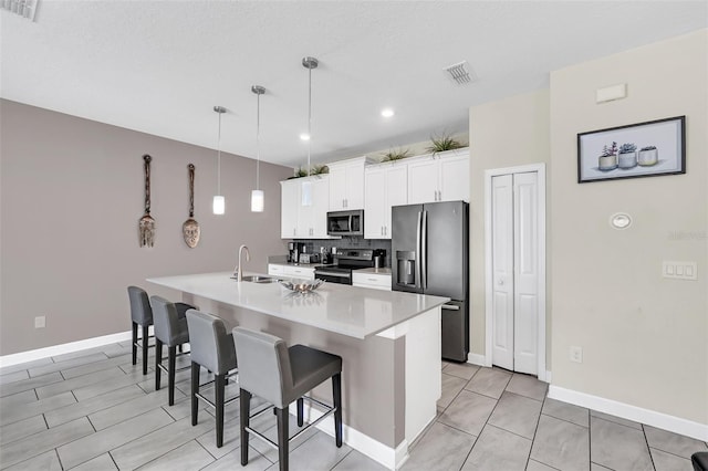 kitchen with appliances with stainless steel finishes, white cabinets, pendant lighting, a kitchen island with sink, and sink