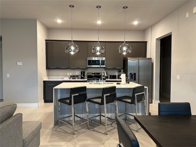 kitchen with appliances with stainless steel finishes, hanging light fixtures, a kitchen island with sink, and a breakfast bar