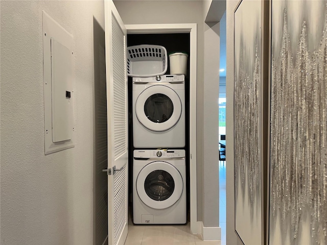 clothes washing area featuring electric panel, light tile patterned flooring, and stacked washing maching and dryer