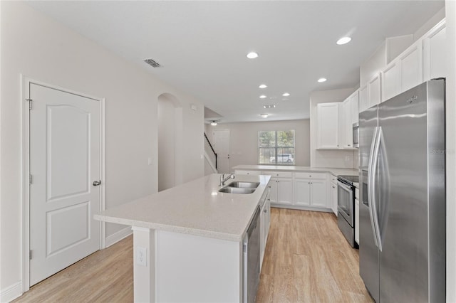 kitchen featuring appliances with stainless steel finishes, white cabinets, light wood-type flooring, a center island with sink, and sink