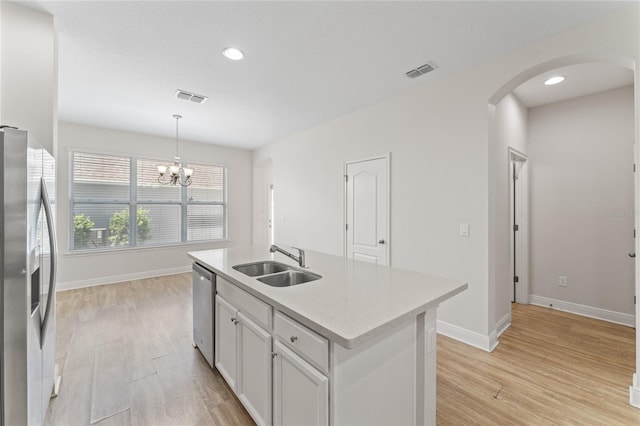 kitchen featuring appliances with stainless steel finishes, light wood-type flooring, a center island with sink, sink, and a notable chandelier