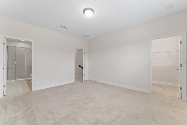 unfurnished bedroom featuring light carpet, a closet, ensuite bath, and a spacious closet