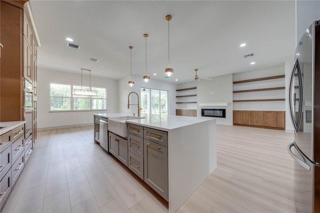 kitchen with ceiling fan, an island with sink, sink, appliances with stainless steel finishes, and a large fireplace