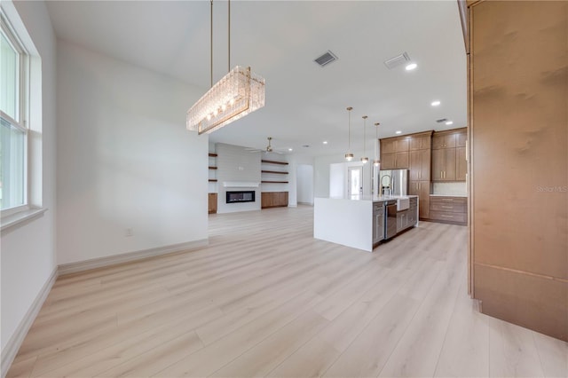 kitchen featuring light wood-type flooring, a center island with sink, stainless steel refrigerator, and decorative light fixtures