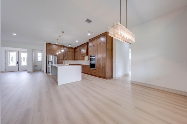 kitchen with pendant lighting, a kitchen island with sink, sink, light hardwood / wood-style flooring, and appliances with stainless steel finishes