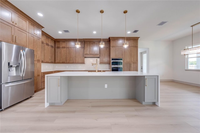 kitchen featuring light hardwood / wood-style floors, tasteful backsplash, an island with sink, appliances with stainless steel finishes, and decorative light fixtures