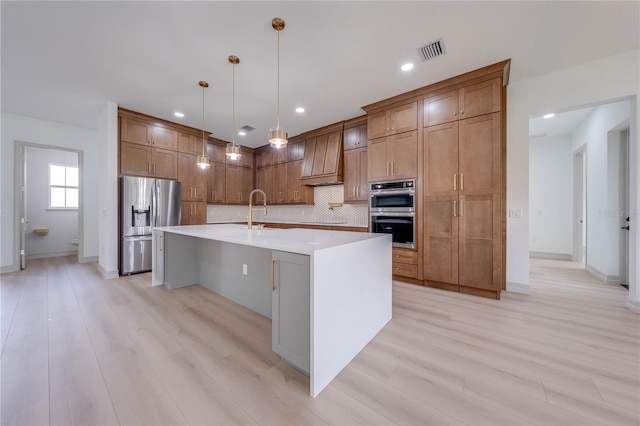 kitchen with an island with sink, light wood-type flooring, appliances with stainless steel finishes, and sink