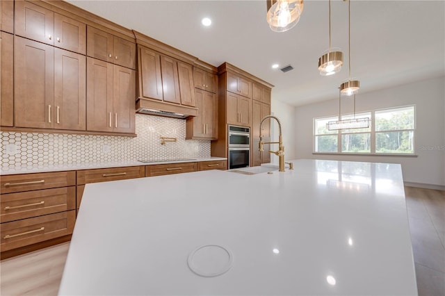 kitchen featuring light hardwood / wood-style flooring, stainless steel double oven, a kitchen island with sink, and sink