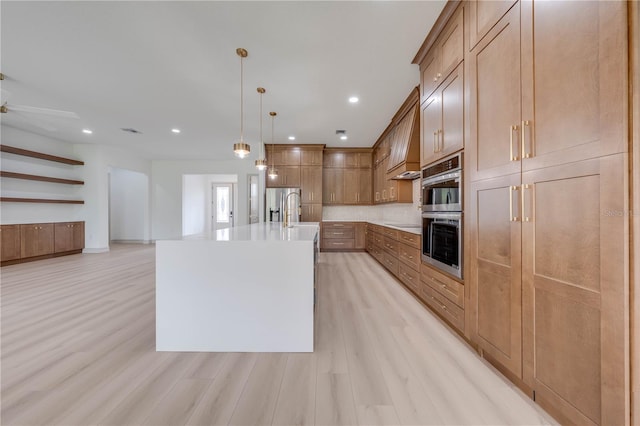 kitchen featuring ceiling fan, pendant lighting, an island with sink, appliances with stainless steel finishes, and light wood-type flooring