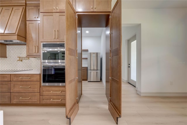 kitchen featuring custom exhaust hood, appliances with stainless steel finishes, backsplash, and light hardwood / wood-style flooring