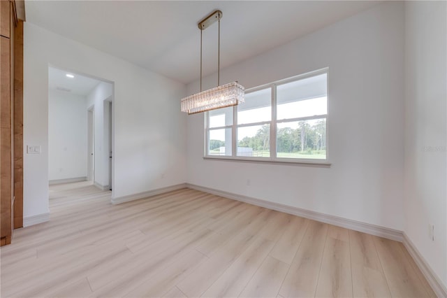 unfurnished room with a notable chandelier and light hardwood / wood-style flooring