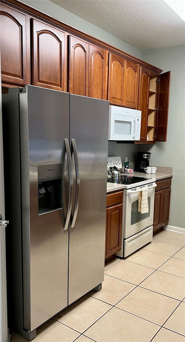 kitchen featuring white appliances, a textured ceiling, and light tile patterned floors