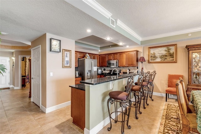 kitchen with visible vents, stainless steel appliances, crown molding, a kitchen bar, and a raised ceiling