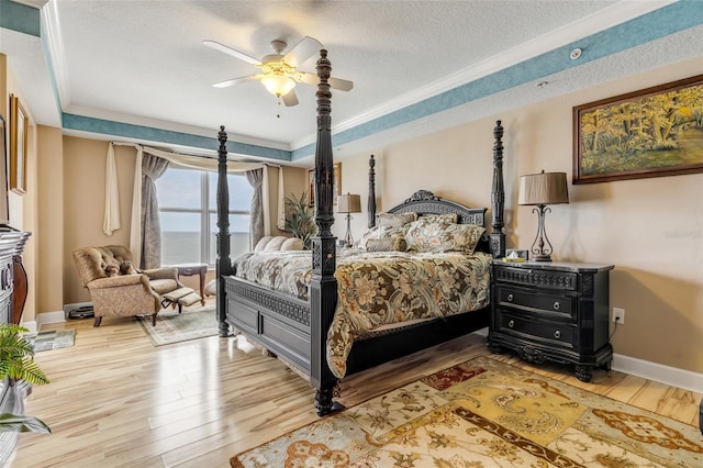 bedroom featuring baseboards, wood finished floors, a textured ceiling, a raised ceiling, and a ceiling fan