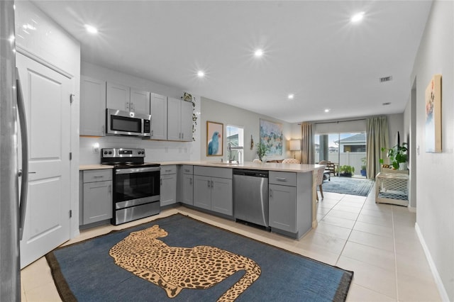 kitchen with gray cabinetry, kitchen peninsula, light tile patterned floors, stainless steel appliances, and sink