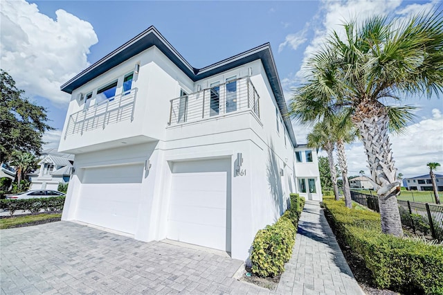 view of side of property with fence, a garage, a balcony, stucco siding, and decorative driveway