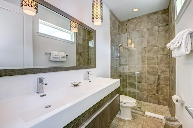 full bathroom featuring a tile shower, toilet, a sink, and double vanity