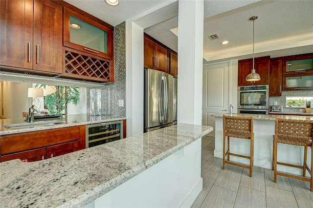 kitchen featuring appliances with stainless steel finishes, a textured ceiling, light stone counters, decorative light fixtures, and wine cooler