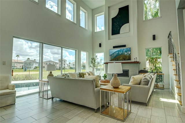 living area featuring stairs, a healthy amount of sunlight, a glass covered fireplace, and a towering ceiling