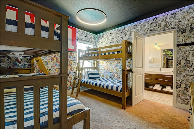 bedroom with a textured ceiling, tile patterned floors, wallpapered walls, connected bathroom, and carpet