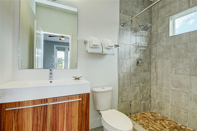 bathroom with tiled shower, vanity, ceiling fan, and toilet