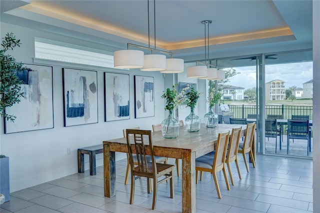 dining space with baseboards, light tile patterned flooring, and a raised ceiling