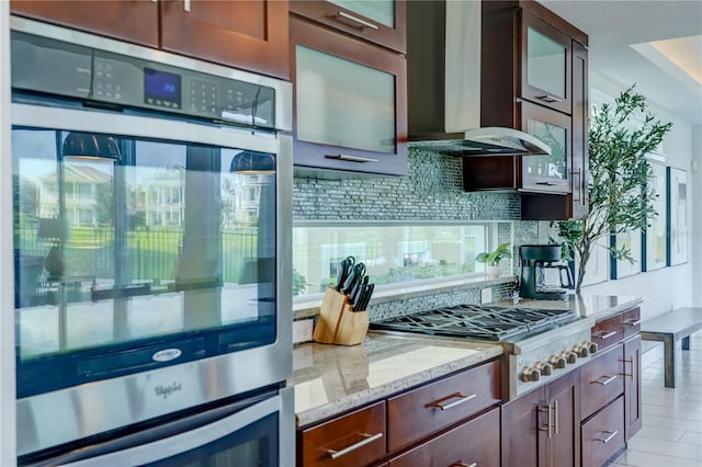 kitchen featuring light stone counters, stainless steel appliances, wall chimney range hood, and tasteful backsplash