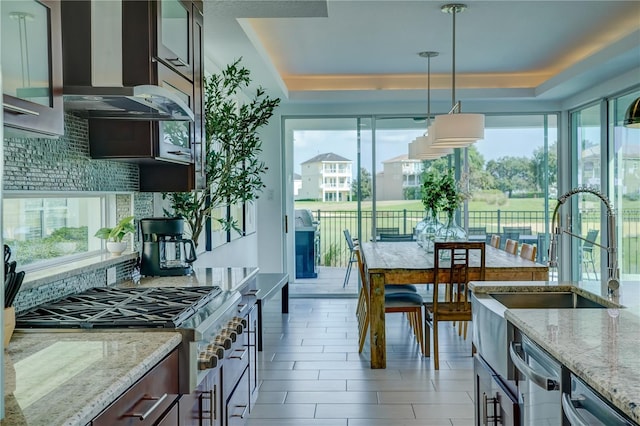 kitchen featuring a tray ceiling, tasteful backsplash, wall chimney exhaust hood, and light stone countertops