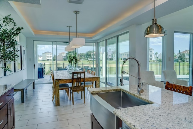 kitchen featuring a raised ceiling, light stone countertops, a wealth of natural light, and pendant lighting