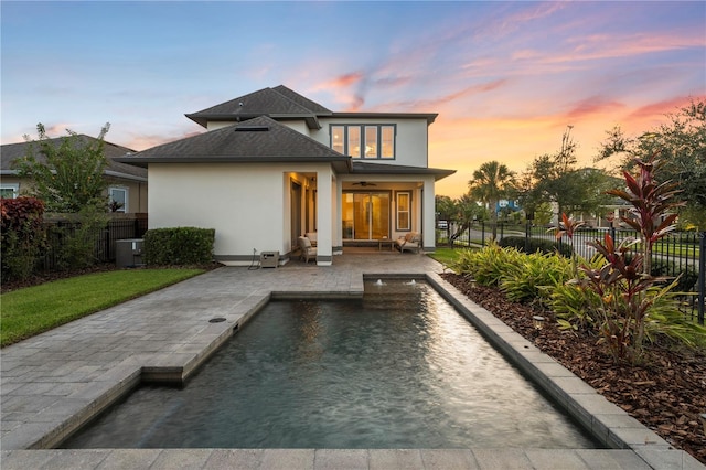 back house at dusk with a fenced in pool and a patio area