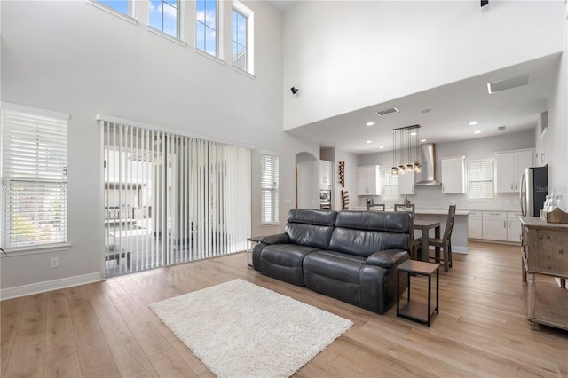 living room featuring light wood-type flooring, a towering ceiling, and a wealth of natural light