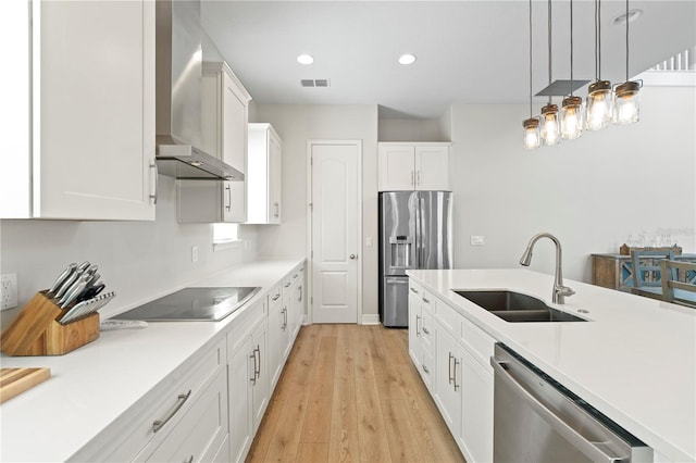 kitchen with white cabinets, sink, decorative light fixtures, wall chimney exhaust hood, and appliances with stainless steel finishes