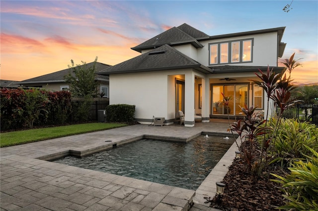 pool at dusk with ceiling fan and a patio area