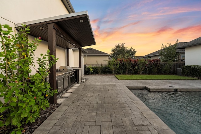 patio terrace at dusk with exterior kitchen, a fenced in pool, and area for grilling