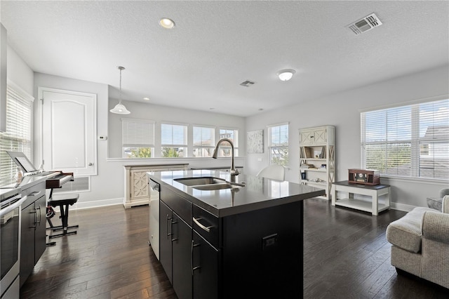 kitchen with a textured ceiling, dark wood-type flooring, a kitchen island with sink, sink, and hanging light fixtures