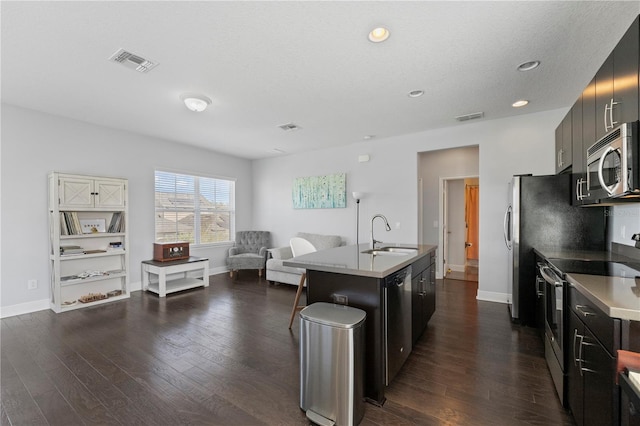 kitchen featuring appliances with stainless steel finishes, dark hardwood / wood-style flooring, a textured ceiling, a kitchen island with sink, and sink