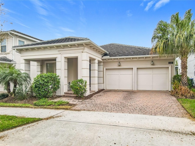 view of front of house with a tiled roof, decorative driveway, an attached garage, and stucco siding