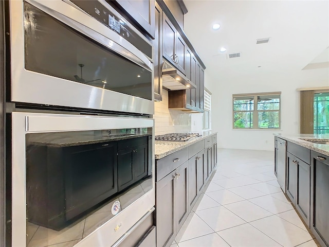 kitchen with light stone counters, visible vents, decorative backsplash, appliances with stainless steel finishes, and under cabinet range hood